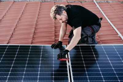 Mature technician man assembling solar panels on house roof for self consumption. renewable energies