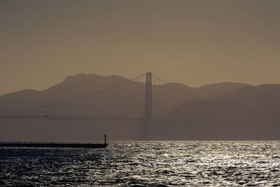 Silhouette of suspension bridge over sea against sky