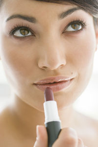 Close-up of beautiful woman looking up while applying lipstick on lips