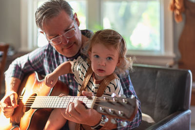 Grandfather teaching guitar to granddaughter at home