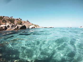 Scenic view of rocks in sea against clear blue sky