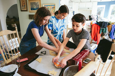 Three siblings cut halloween shaped cookies out of dough