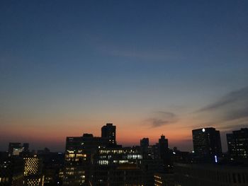 Illuminated buildings in city against sky during sunset