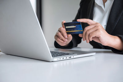 Midsection of businesswoman holding credit card by laptop on table