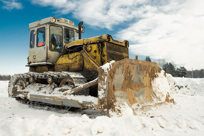 Yellow crawler tractor bulldozer with a bucket works in winter clearing the road from snow. 