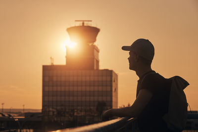 Traveler with backpack at airport. silhouette of man against air traffic control tower at sunset.