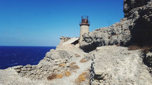 Lighthouse by sea against clear blue sky