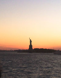 Statue of liberty by sea against sky at dusk