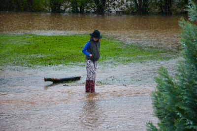 Full length of girl standing by flood in the water, after raining 