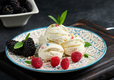 Three scoops of white ice cream in a round plate with mint leaves on a black table