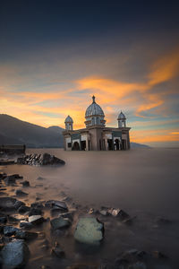 Built structure by sea against sky during sunset