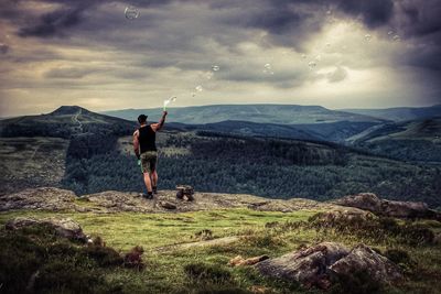 Rear view of man standing on mountain against sky