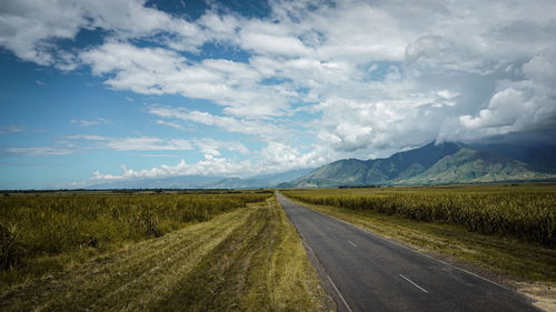 Empty road amidst field against sky