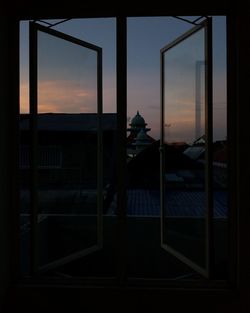 Silhouette person outside house against sky during sunset