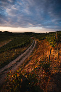 Empty road amidst field against sky during sunset