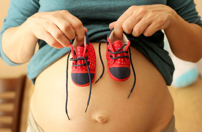 Midsection of pregnant woman holding baby booties on abdomen