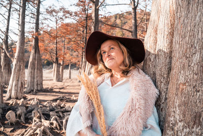 Portrait of woman standing by tree trunk in forest