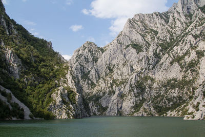 Scenic view of sea by mountain against sky