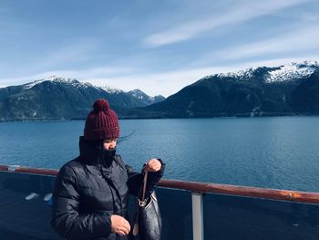 Woman standing by railing over lake against mountains and sky