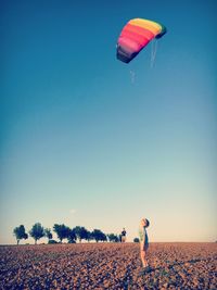 Boys flying colorful kite on field against clear sky