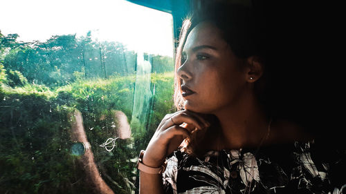 Close-up portrait of young woman looking away against window