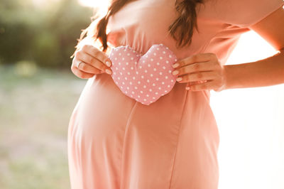 Pregnant woman holding pink heart outdoors. maternity. motherhood.