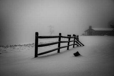 Bench on snow covered field against sky