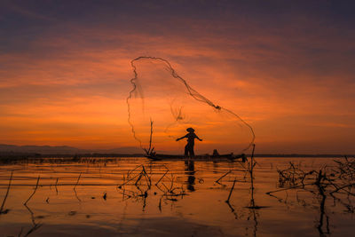 Silhouette people standing by sea against sky during sunset