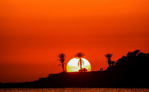 Silhouette palm trees by sea against romantic sky at sunset