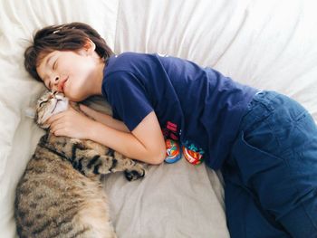 Overhead view of boy cuddling a cat on a bed