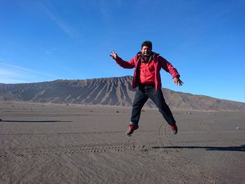 Full length of man jumping at desert against blue sky