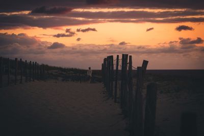 Wooden posts on beach against sky during sunset