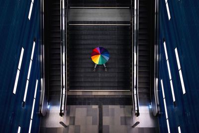 High angle view of person with multi colored umbrella sitting on steps in illuminated building