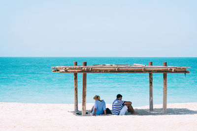 Friends sitting on beach against clear sky