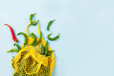 Creative layout green chilli peppers in yellow string bag on pastel blue background