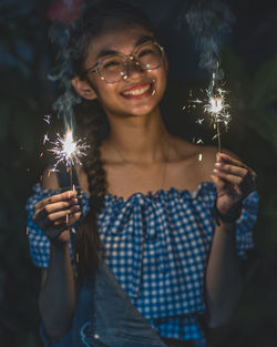 Portrait of young woman holding sparkler at night