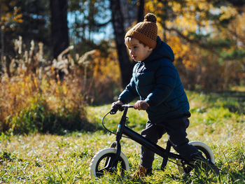 Cute toddler boy in casual clothes riding on balance bike in autumn forest