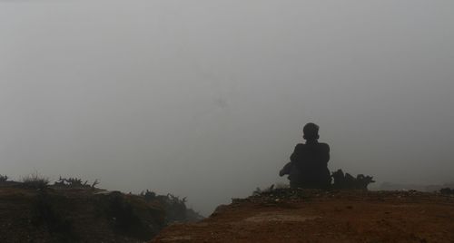 Silhouette people on land against sky during foggy weather