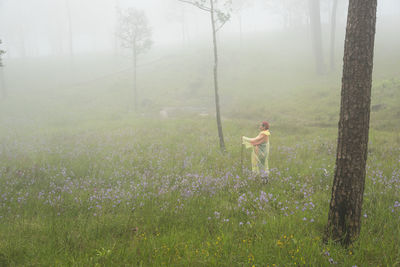 Side view of woman standing on grassy field during foggy weather