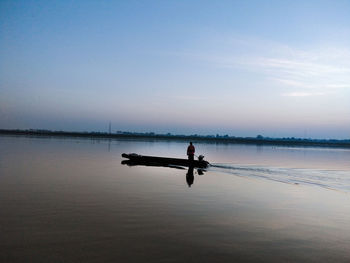 Silhouette man on boat in lake against sky