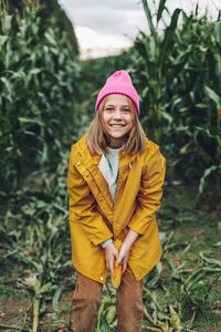 Funny little girl dressed in a yellow raincoat and a hot pink cap spoils and bites corn 