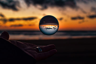 Close-up of hand against sea at sunset