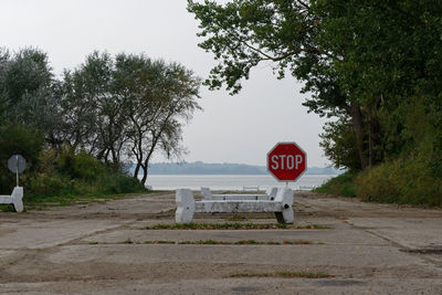 Road sign by trees against sky