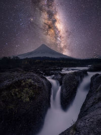 Scenic view of waterfall by mountains against star field at night