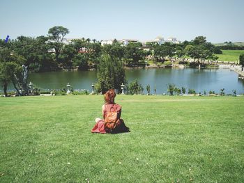 Rear view of woman sitting on grassy field at buddha eden garden