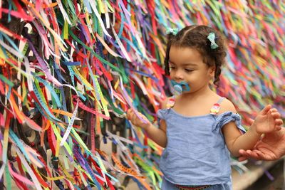 Cute girl sucking pacifier by multi colored ribbons