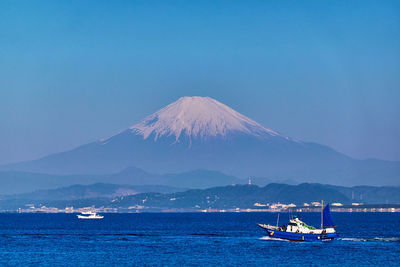 Scenic view of sea and snowcapped mountain against clear blue sky