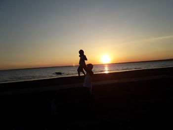 Silhouette of man standing on beach against sky during sunset