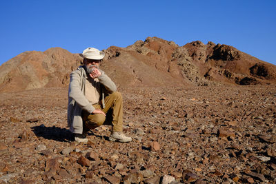 Senior man sitting on rock against clear sky at desert 
