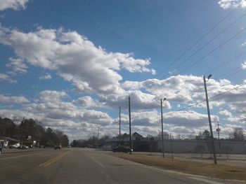 Road by electricity pylon against sky